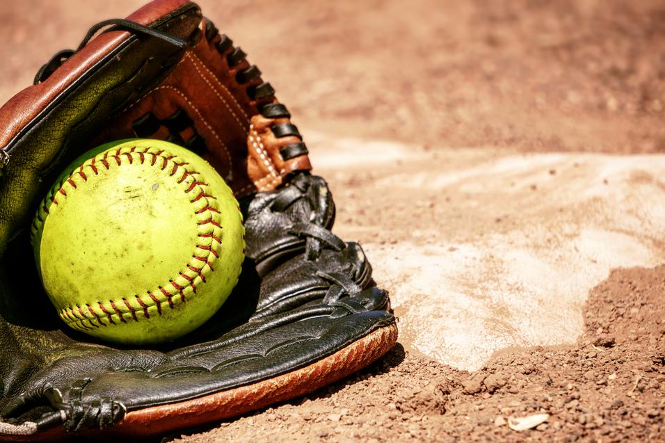 Nahaufnahme eines Softballs in einem Baseballhandschuh auf einem Erdboden.