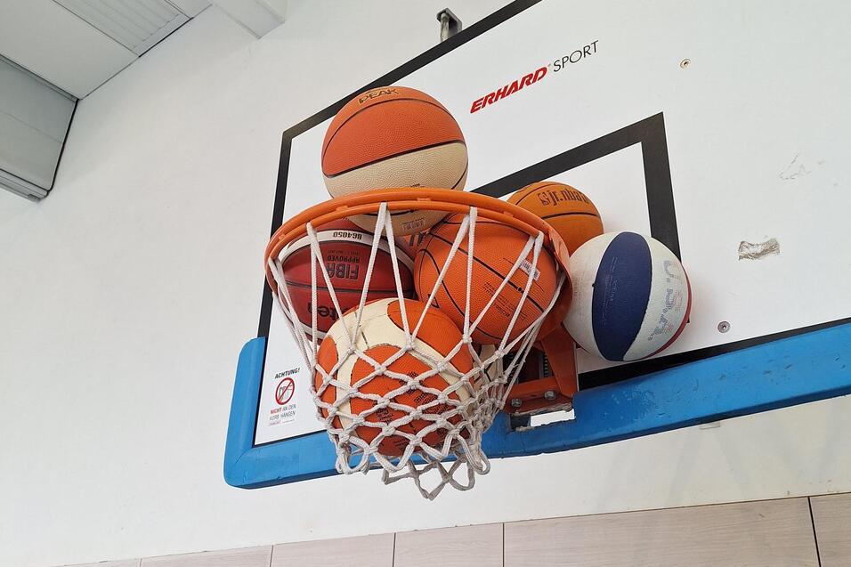 Mehrere Basketballs liegen übereinander im Netz eines Basketballkorbs an einer Wand.