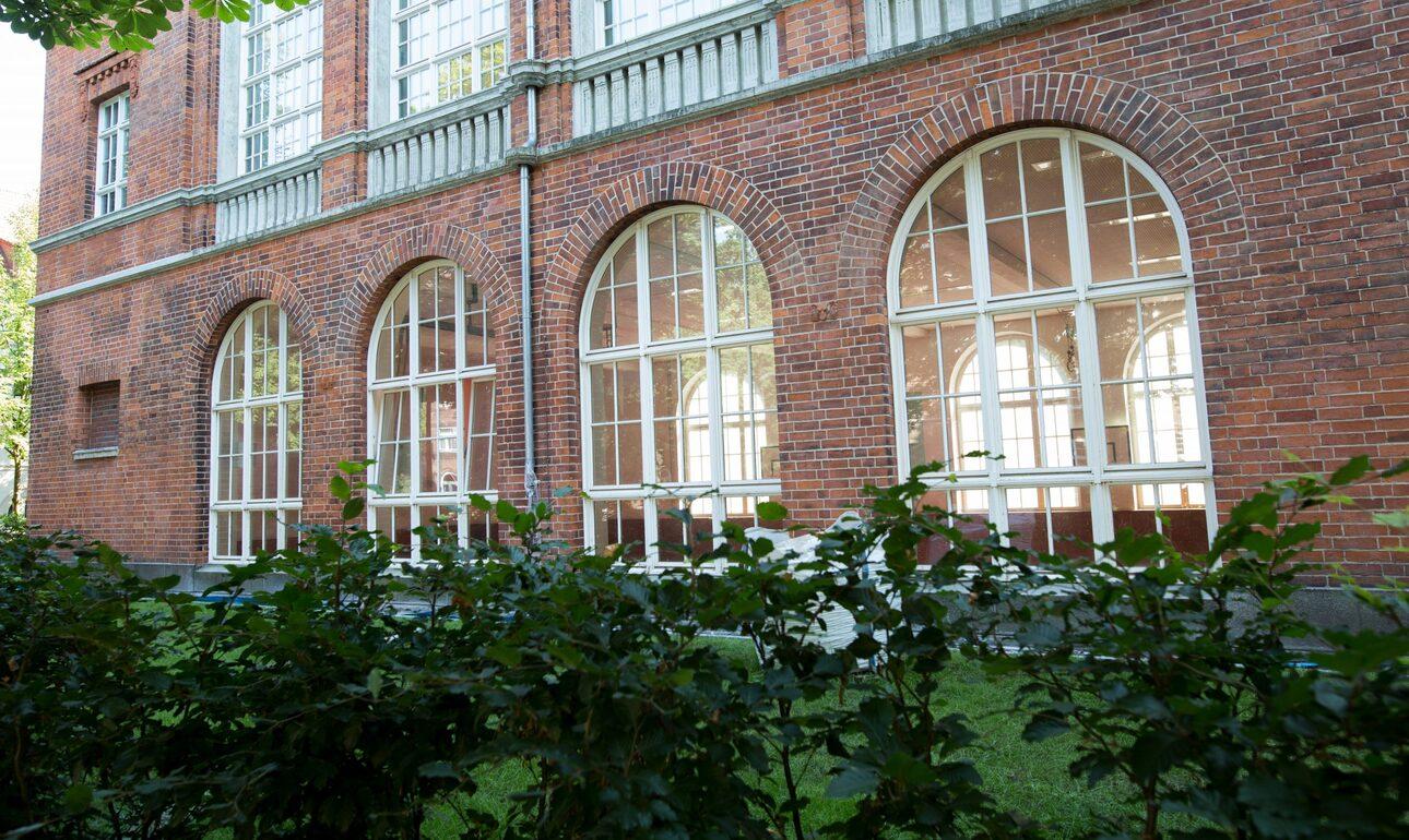 Historisches Backsteingebäude mit großen, runden Fenstern, umgeben von einem grünen Garten.