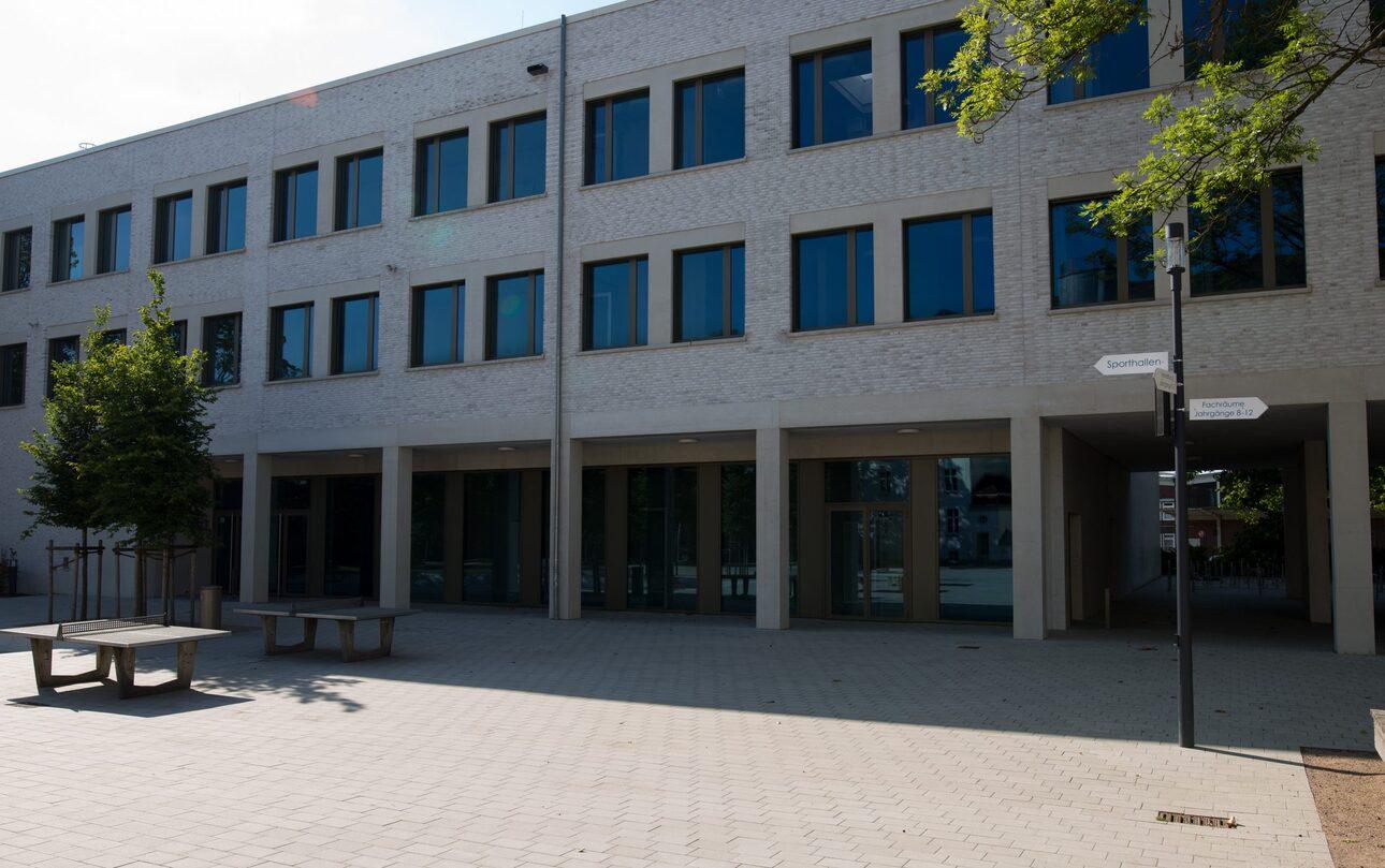 Fassade eines modernen Gebäudes mit großen Fenstern, einem Platz mit Sitzgelegenheiten und einem Verkehrsschild.