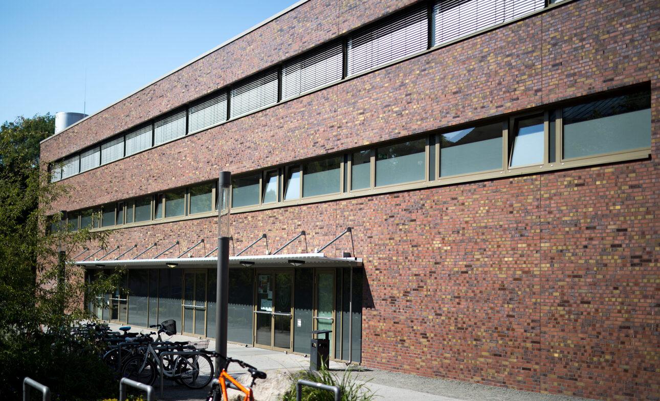 Fassade eines modernen, zweigeschossigen Gebäudes mit großen Fenstern und Fahrradparkplätzen im Vordergrund.