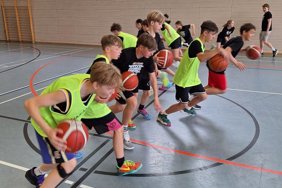 Gruppe von Jungen in grünen Trainingswesten dribbelt Basketballs in einer Sporthalle.