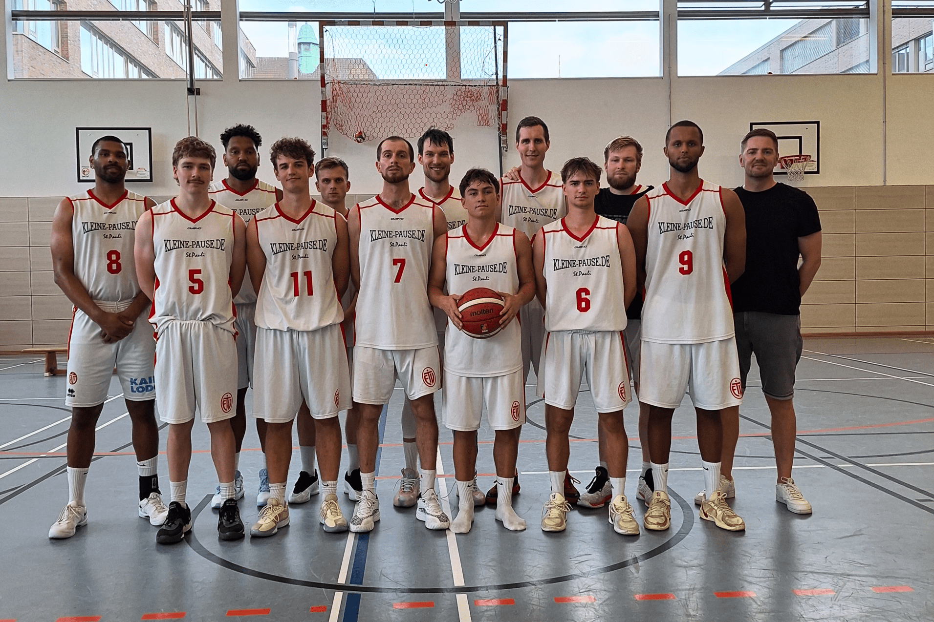 Mannschaftsfoto einer Basketballmannschaft mit 12 Spielern in weißen Trikots auf einem Basketballfeld.