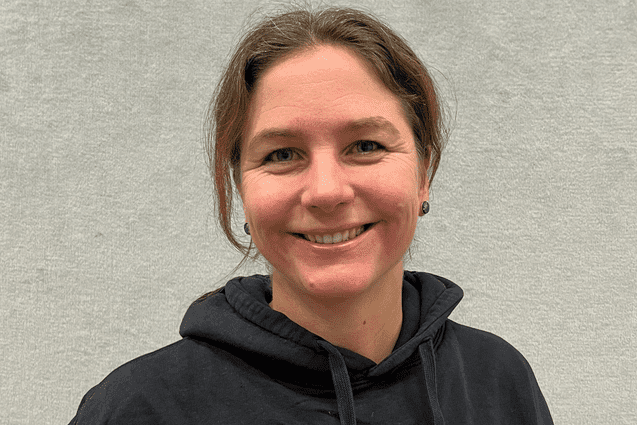 Lächelnde Frau mit kurzen Haaren in schwarzem Hoodie mit Aufschrift „ETV HAMBURG BASKETBALL“ vor grauem Hintergrund.