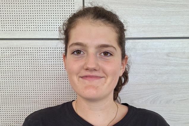 Porträt einer lächelnden jungen Frau in schwarzem T-Shirt mit Basketballmotiv vor hellen Holzpanelen.