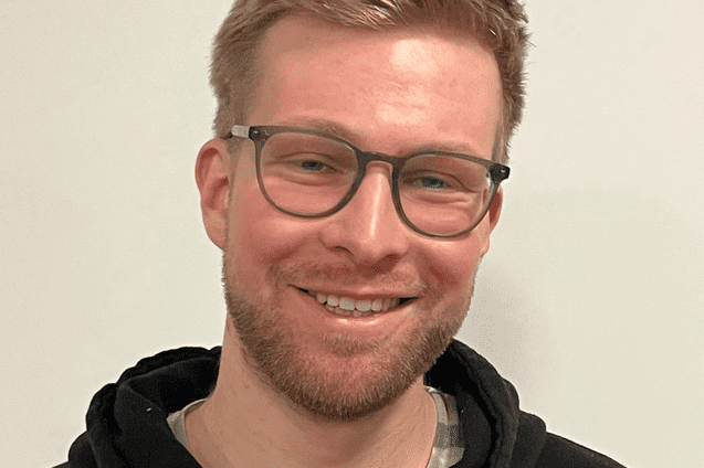 Lächelnder Mann mit Brille und blonder Stoppelfrisur trägt einen schwarzen Hoodie mit der Aufschrift "Hamburg Basketball".