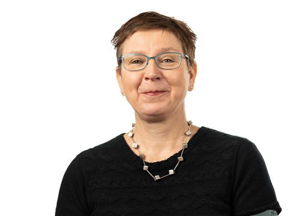 Porträt einer lächelnden Frau mit Brille, kurzem Haar und einer Kette, die auf einem weißen Hintergrund steht.
