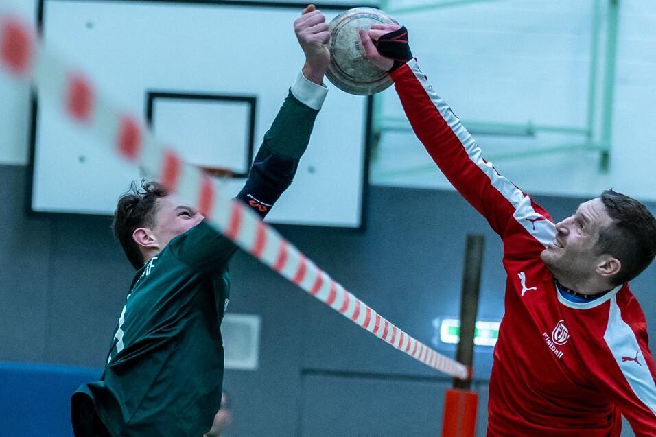 Zwei Handballspieler im Wettkampf, ein Spieler springt mit Ball, während der andere abwehren möchte.