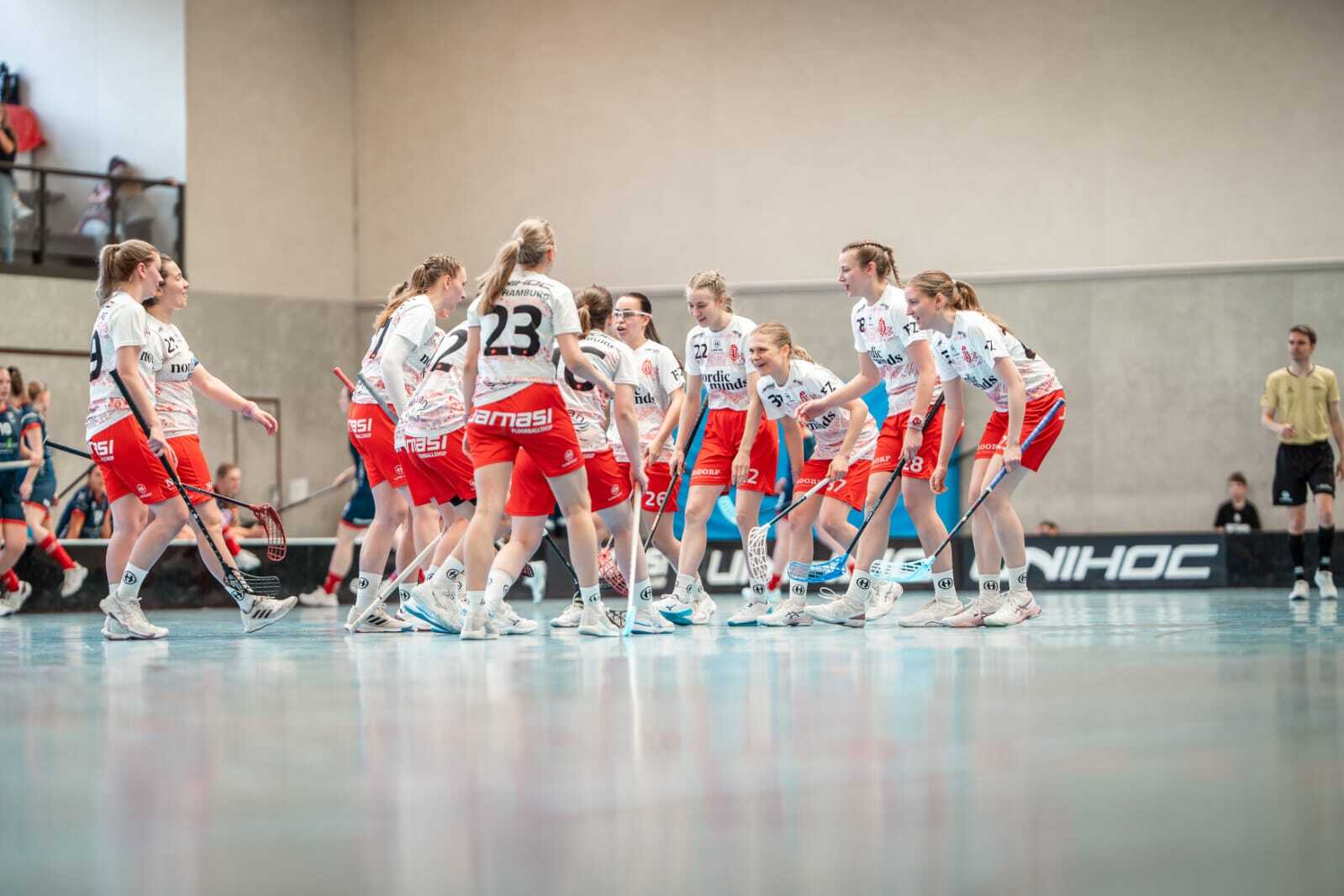 Gruppenbild von Spielerinnen eines Floorball-Teams in roten Shorts und weißen Shirts, die sich auf das Spiel vorbereiten.