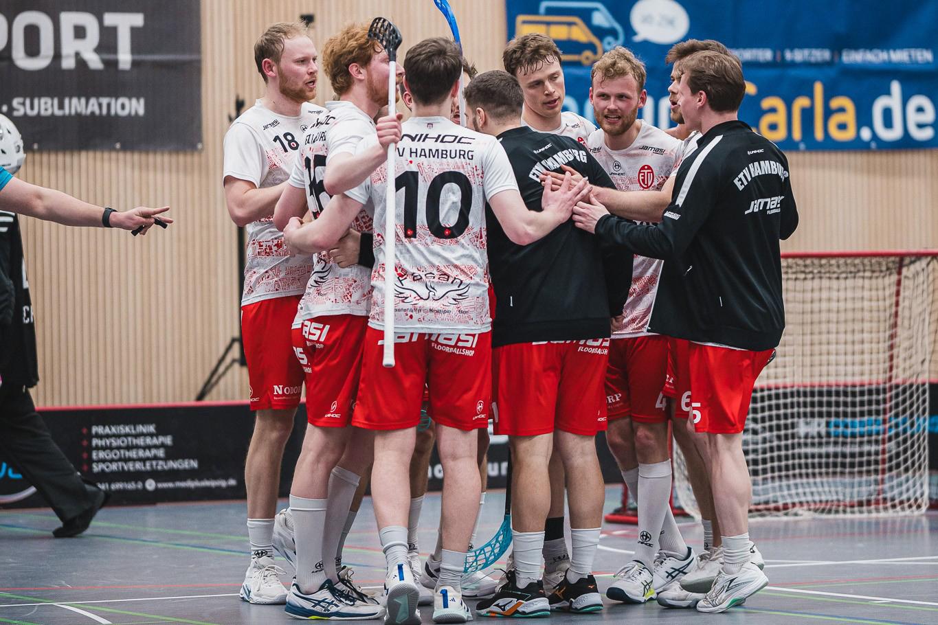 Eine Gruppe von sechs männlichen Floorballspielern in roten Trikots umarmt sich in einer Sporthalle.