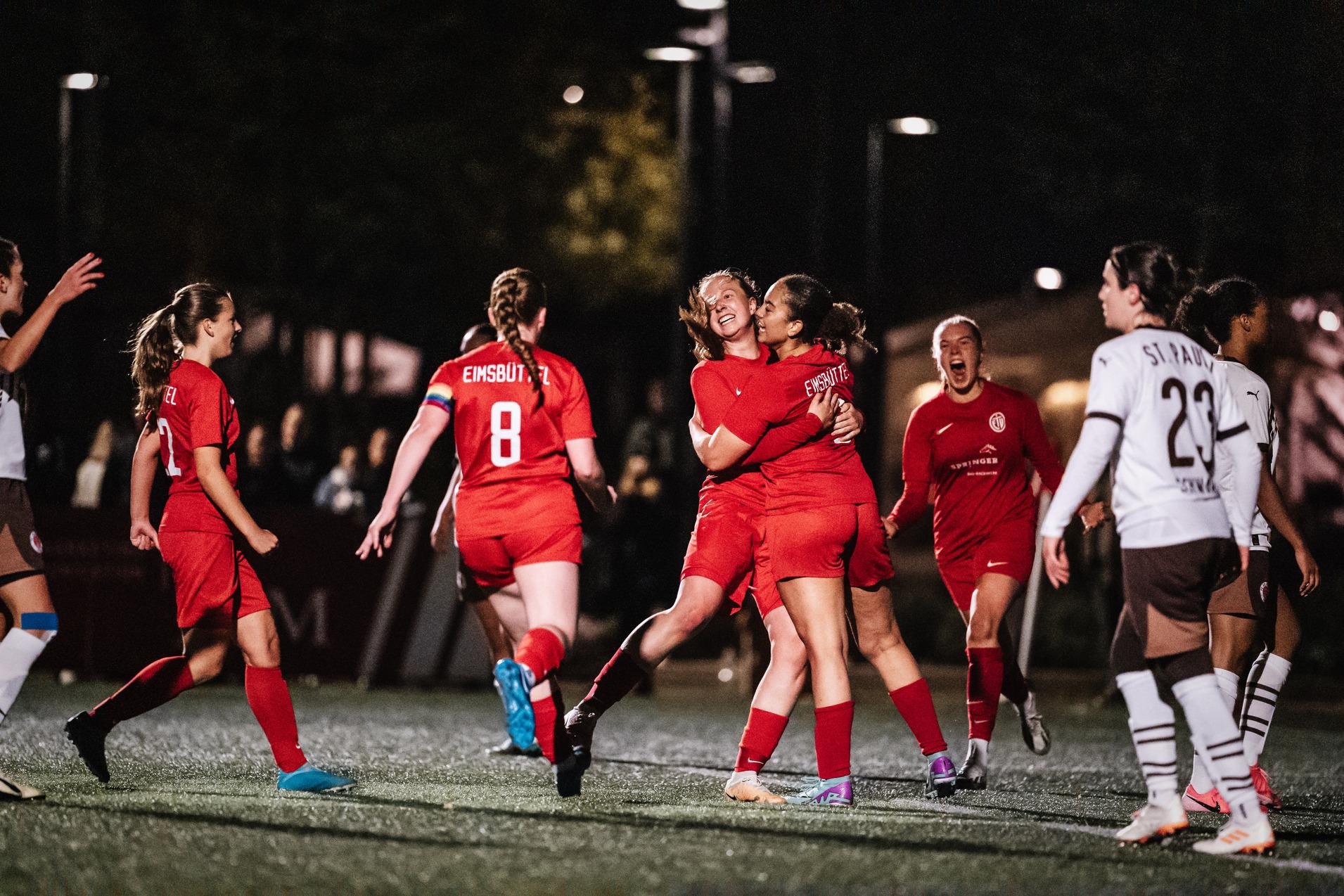 Gruppenszenen von feiernden Fußballspielerinnen in roten Trikots auf einem Kunstrasenplatz bei Nacht.