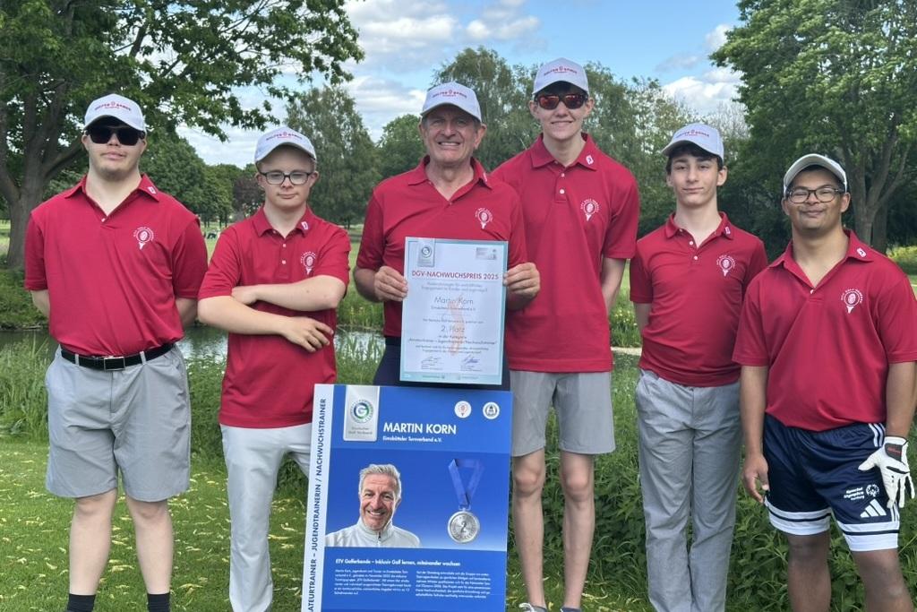 Sechsköpfige Gruppe in roten Poloshirts posiert neben einer Urkunde und einem Informationsschild auf einem Golfplatz.