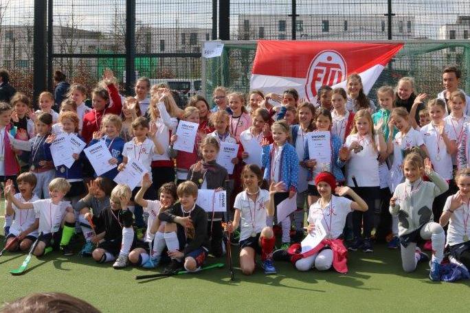 Gruppenshot von vielen Kindern mit Medaillen und Urkunden auf einem Hockeyplatz, im Hintergrund ein Fahne des Vereins.