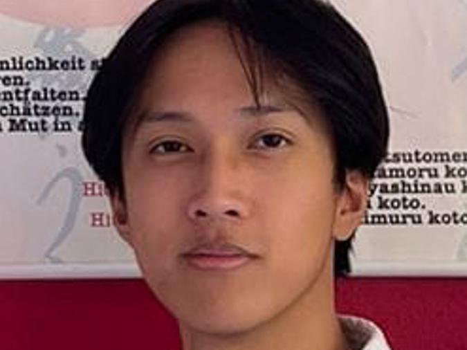 Porträt eines jungen Mannes im Karateanzug vor einer Wand mit japanischen Schriftzeichen.