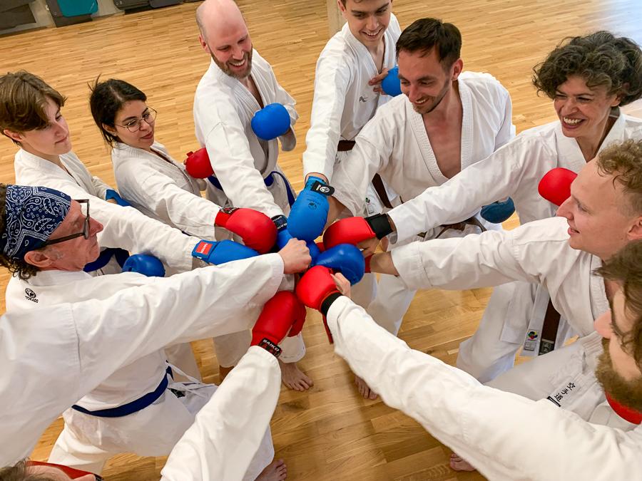 Gruppe von Karateka in weißen Gi, die fröhlich farbige Boxhandschuhe zusammenschlagen.