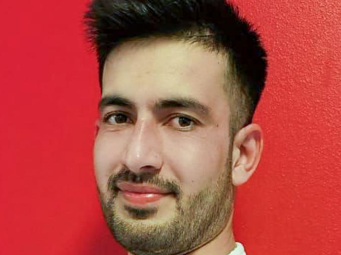 Porträt eines Mannes in einem weißen Karateanzug vor roter Wand, mit kurzem Bart und lächelndem Gesichtsausdruck.
