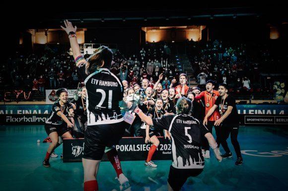 Feiernde Spielerinnen von ETY Hamburg jubeln nach ihrem Pokalsieg, umgeben von einer jubelnden Zuschauermenge.