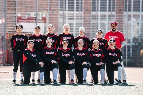 Mannschaftsfoto der Softballmannschaft "Knights" mit Spielern und Trainer auf einem Sportplatz. Alle tragen einheitliche Trikots.