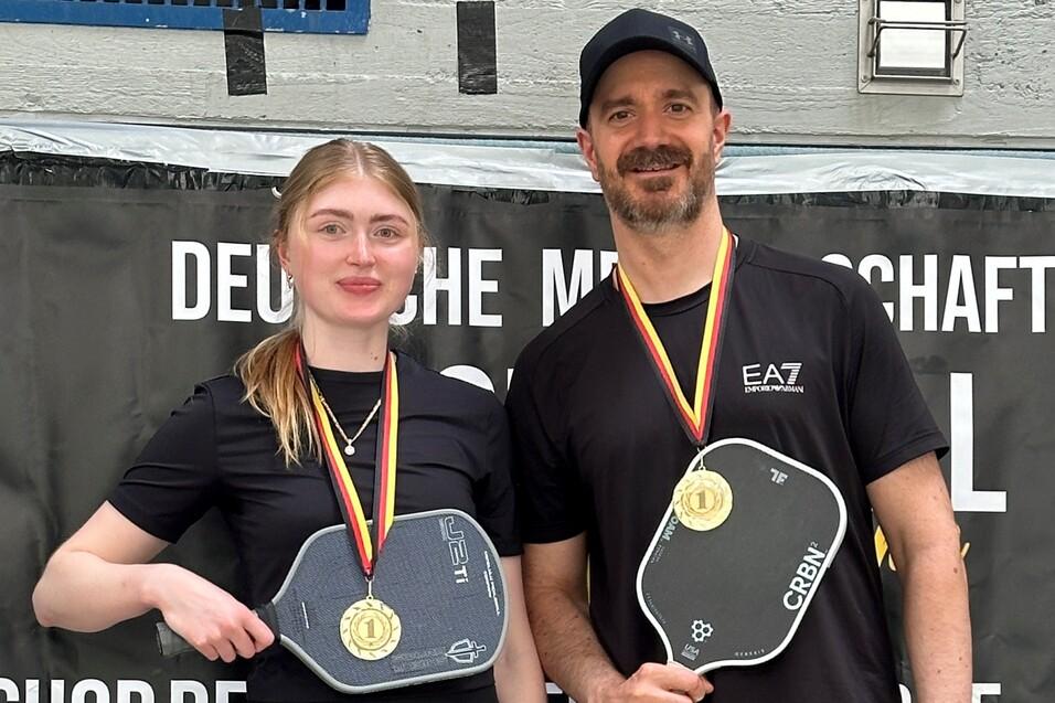 Zwei Medaillengewinner halten Pickleball-Schläger in der Hand und stehen vor einem Banner mit dem Schriftzug „DEUTSCHE MEISTERSCHAFTEN“.