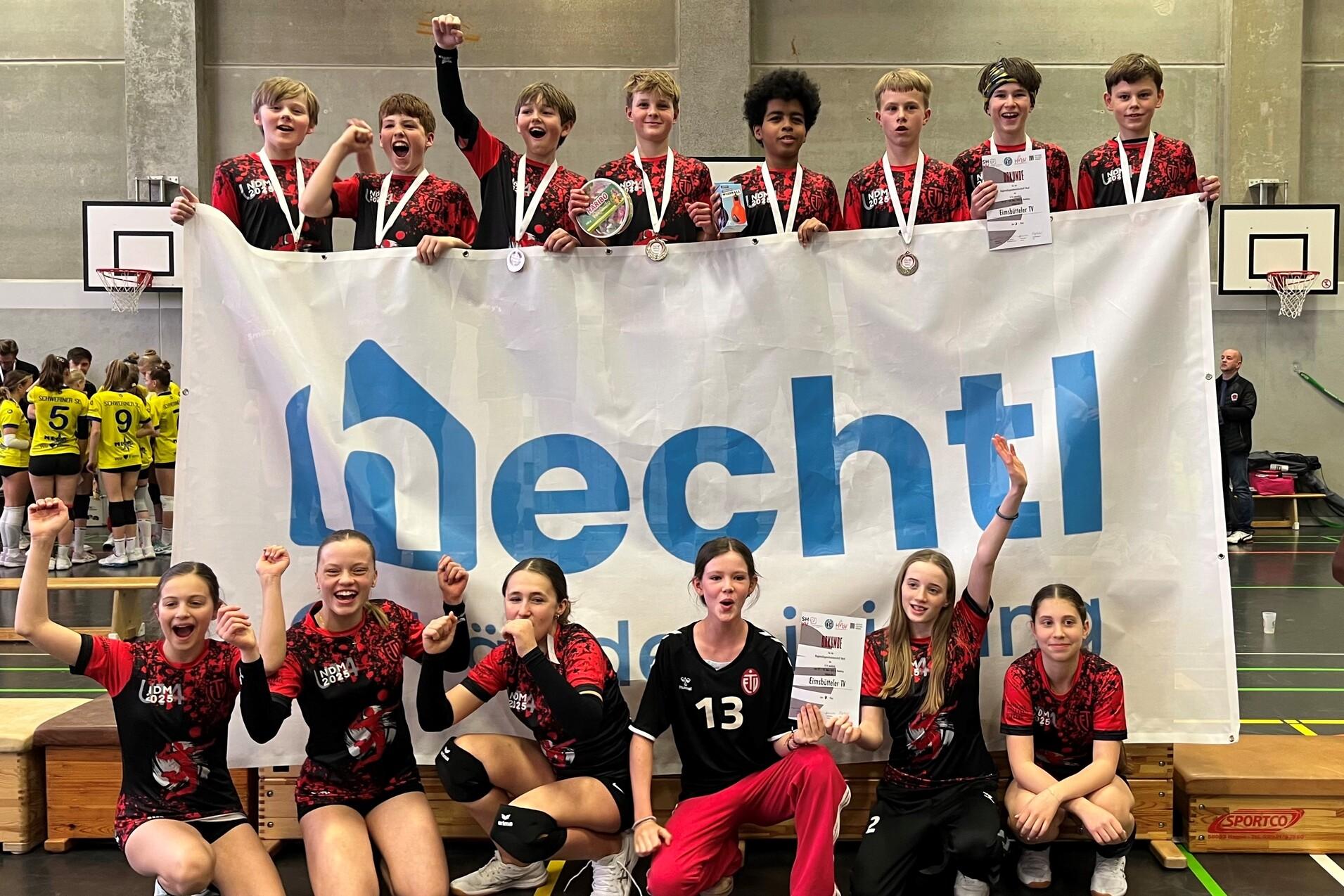 Gruppenshot von jungen Sportlern mit Medaillen, die vor einem Banner jubeln und einen Pokal in der Hand halten.
