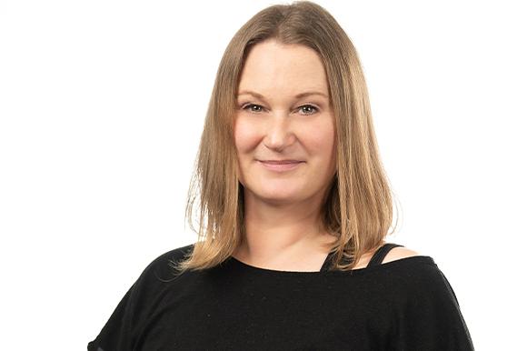 Porträt einer lächelnden Frau mit langen, glatten Haaren, die ein schwarzes Shirt trägt, vor einem weißen Hintergrund.