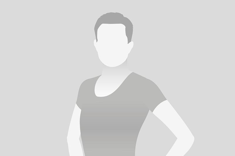 Porträt einer Person mit neutralem Gesichtsausdruck in einem schlichten, grauen Hintergrund.