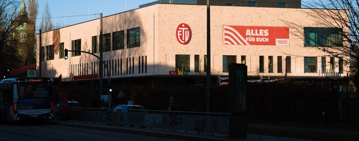 Fassade eines modernen Gebäudes mit einem Logo und einem großen Banner, beschriftet mit „ALLES FÜR EUCH“.