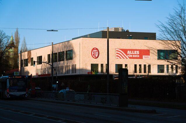 Fassade eines modernen Gebäudes mit dem Logo des ETB und einem Banner „ALLES FÜR EUCH“ in der Abendsonne.
