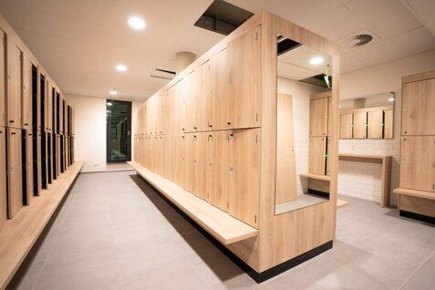 Sportzentrum Hoheluft Umkleide Modernes Umkleideraum mit Holzkabinen, Sitzbank und Spiegeln auf hellgrauem Boden. Sanfte Beleuchtung.