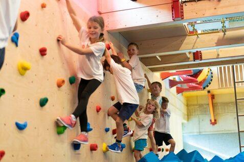 Sportzentrum Hoheluft Kletterwelt Sechs Kinder klettern an einer bunten Kletterwand in einem Indoor-Spielplatz.