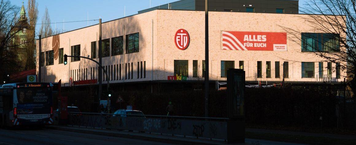 Fassade eines modernen Gebäudes mit dem Logo des ETB und einem Banner „ALLES FÜR EUCH“ in der Abendsonne.