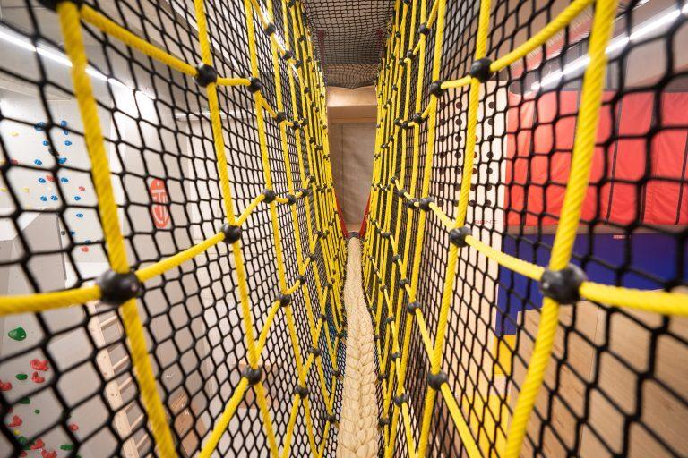 Blick auf ein Klettergerüst mit gelben Netzen und einem Seil in einem Indoor-Spielbereich.