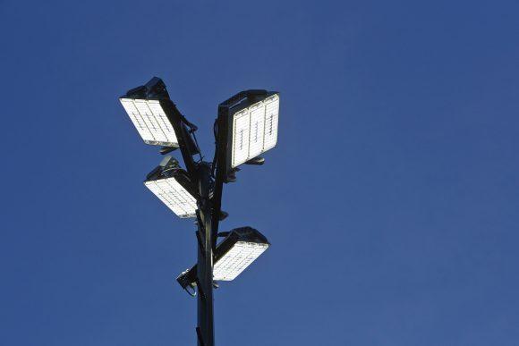 Vier LED-Straßenleuchten montiert auf einem hohen Mast vor klarem blauen Himmel.