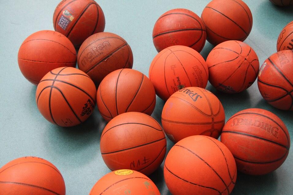 Ansammlung von orangefarbenen Basketballen auf einer grünen Unterlage, verschiedene Marken und Größen sichtbar.