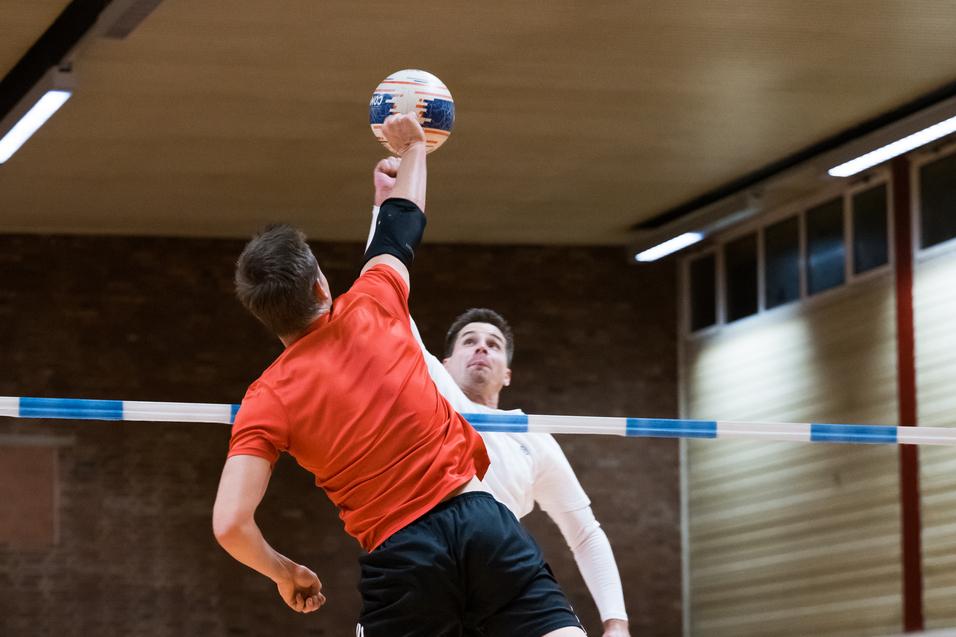 Zwei Spieler im Sprung während eines Handballspiels, einer wirft den Ball über eine Markierung.