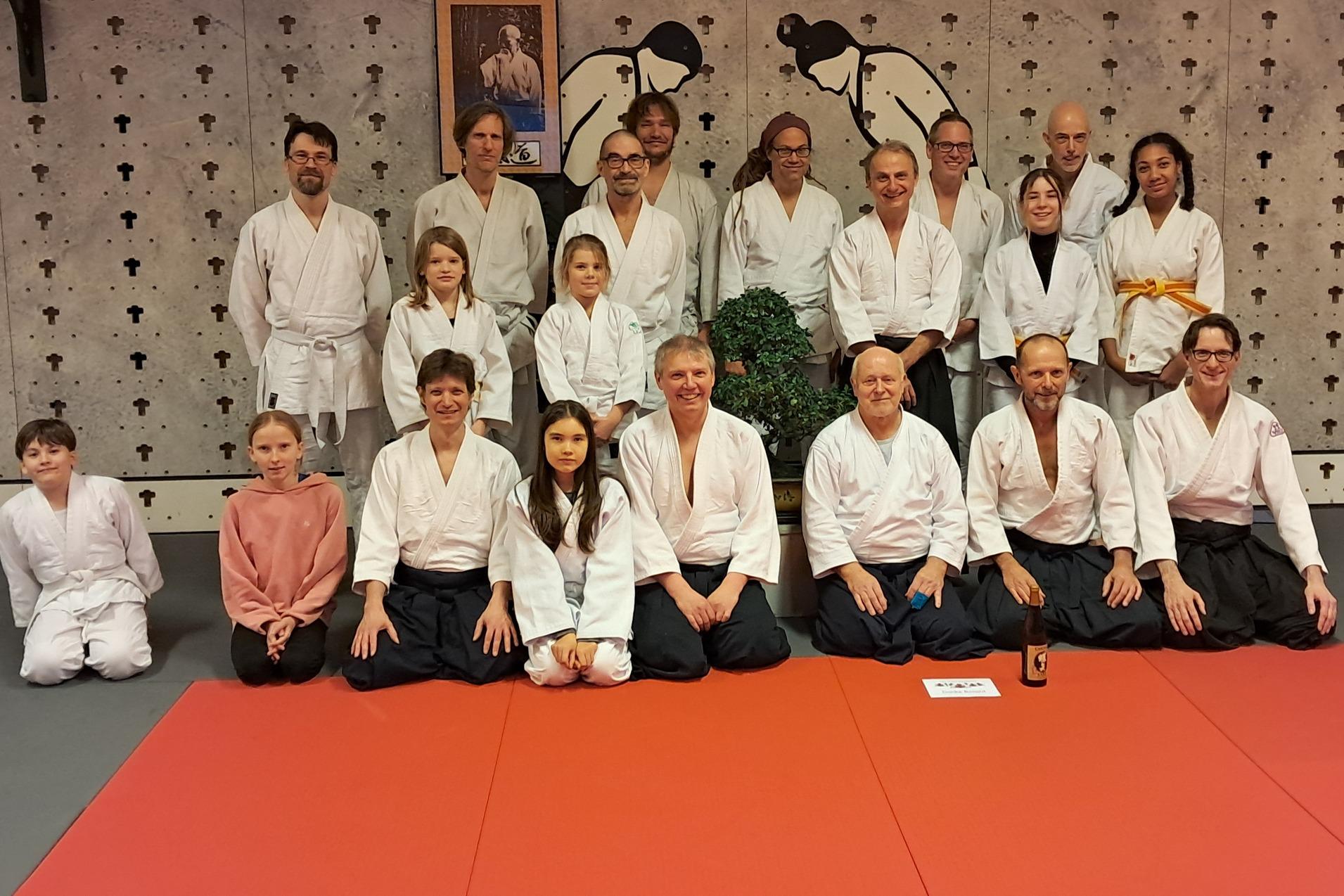 Gruppenfoto von 20 Personen in Karate-Anzügen auf einer roten Matte in einem Dojo mit einer Wandmalerei im Hintergrund.